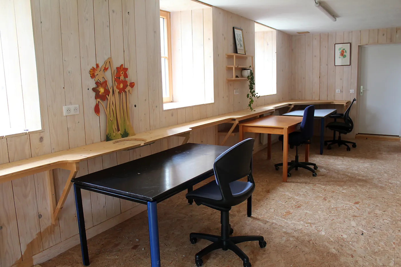 Un bureau face à un mur en bois clair, entre deux fenêtres donnant sur la verdure.